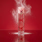 Angle : Au niveau du sol (Eye-level / Ground shot).  Scène : Le flacon de parfum est posé à la verticale sur un miroir parfait. Un léger nuage de sucre glace blanc est capturé en plein mouvement, saupoudrant l'air autour du bouchon rose et rouge. Le contraste entre le rouge vibrant des lignes du flacon et la blancheur du sucre crée un effet visuel saisissant.  Fond : Un arrière-plan monochrome rouge carmin mat, ultra-propre et moderne. (gemini-3.1-flash-image-preview)