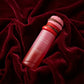 Angle : Vue à 30 degrés vers le bas.  Scène : Le flacon de parfum repose incliné, presque couché, au creux d'un drapé sculptural fait de tissu en velours lourd couleur rouge cerise foncé. Les plis du tissu s'enroulent harmonieusement autour de la base et du bouchon pour créer un écrin de douceur absolue.  Décor & Lumière : Le tissu remplit l'intégralité du cadre. Une lumière directionnelle douce (softbox) glisse sur les vagues de velours pour créer un jeu de textures mats et de reflets profonds et luxueux. 