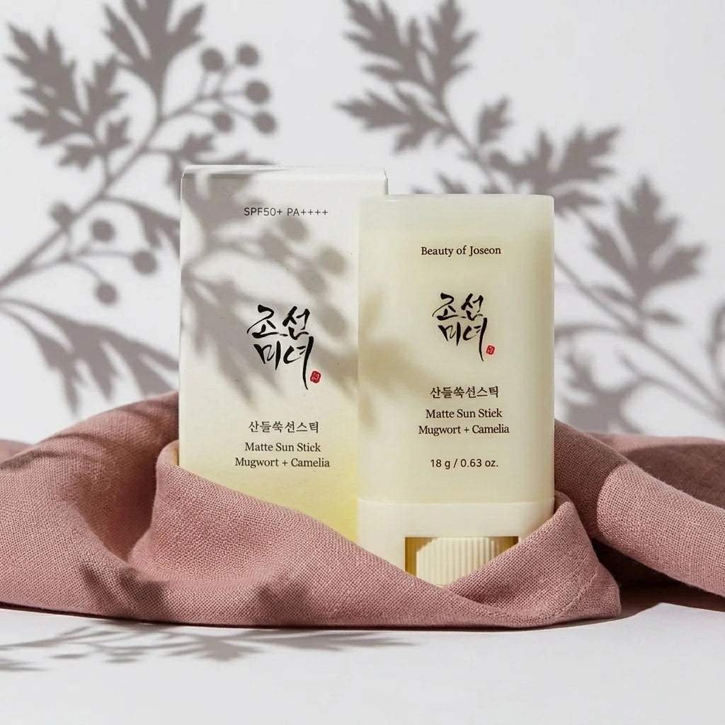 Une prise de vue frontale épurée et géométrique. Le stick solaire fermé et son packaging de l'image sont positionnés au centre Exact du cadre, debout. Leur base est délicatement enveloppée par un drapé de tissu de lin lourd couleur vieux rose poudré.  Détails : Fond monochrome blanc mat. Une lumière de studio directionnelle crue vient de biais de manière ciblée, projetant une ombre chinoise floue, poétique et parfaitement découpée de feuilles d'armoise et de baies sur le mur du fond et en superposition sur 