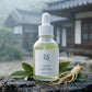 L'Angle : Vue de trois-quarts légèrement en contre-plongée, pour donner de la noblesse au produit.  Le Fond : Une surface en pierre volcanique rugueuse (rappellant l'île de Jeju). La bouteille est entourée de quelques feuilles de thé vert séchées et entières, et d'un petit morceau de racine de ginseng frais (ingrédient secondaire signature).  Atmosphère : Matinal, frais.  Le Prompt :  High-end commercial photography of a Beauty of Joseon Calming Serum bottle (as seen in image_1.png). Low-angle view to give 