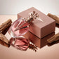 Un plan moyen en plongée à 60 degrés du flacon sculptural de image_2e6623.jpg couché délicatement sur une surface miroir d'or rose parfaitement polie. Le miroir crée une réflexion symétrique, nette et impeccable de la couronne et de la forme effilée de la bouteille de image_2e6623.jpg. Quelques morceaux de bois de santal brut entourent le flacon. La lumière blanche diffuse souligne la complexité du design métallique mat. Style : Photographie éditoriale de beauté. (gemini-3.1-flash-image-preview)