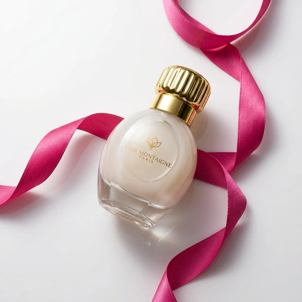 Un plan moyen en plongée à 60 degrés du flacon de image_2fcb00.jpg délicatement posé sur une surface lisse blanche. Un ruban de soie fluide couleur rose fuchsia ondule de manière asymétrique autour de la bouteille. La lumière rasante souligne la rondeur parfaite du flacon de image_2fcb00.jpg et l'éclat miroir de son bouchon métallique doré. Style : Éditorial de beauté épuré et coloré. (gemini-3.1-flash-image-preview)