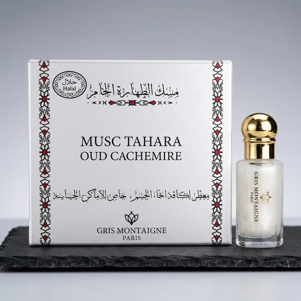 Un plan moyen net et frontal du parfum 'MUSC TAHARA OUD CACHEMIRE' s'inspirant de image_54.jpg. Le grand coffret blanc carré aux frises rouges et lettrages noirs est posé à la verticale sur une dalle texturée d'ardoise noire mate. Juste à côté, à droite, le petit flacon transparent au jus blanc laiteux et pailleté se dresse fièrement, coiffé de son bouchon sphérique en or poli miroir. Éclairage de studio blanc, doux et diffus, éliminant les ombres dures. Style publicitaire épuré et luxueux. (gemini-3.1-flas