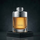 Un portrait de produit épuré et masculin au format carré 1200x1200px. Le flacon de "Bentley For Men" de image_85b966.jpg est posé à la verticale de face au centre d'un bloc géométrique recouvert de cuir noir surpiqué de fil argenté. Le fond est un mur gris de béton ciré très sombre. Une lumière latérale dramatique (chiaroscuro) crée des reflets nets sur les épaules métalliques argentées de la bouteille et illumine le jus ambré chaleureux à travers le verre lourd. Le lettrage "FOR MEN" est d'une netteté abso