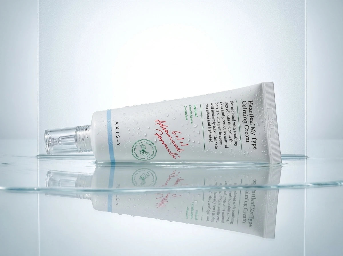 Angle : Prise de vue au ras du support, l'objectif effleurant la surface.  Scène : Le tube est posé horizontalement ou légèrement incliné au centre d'une fine nappe d'eau cristalline. Des micro-gouttelettes de condensation fraîches sont pulvérisées sur le tube blanc mat pour évoquer une hydratation immédiate et un effet rafraîchissant sur la peau.  Fond & Lumière : L'arrière-plan est un panneau de verre dépoli rétroéclairé par une lumière blanche et purifiante. L'eau crée un reflet parfait et net des écritu