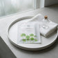 Angle : Vue à $30^\circ$ vers le bas.Scène : Le sachet de Beauty of Joseon est mis en scène sur un plateau rond en céramique mate blanche. À côté du produit, une serviette d'invité en coton nid d'abeille blanche ultra-texturée est pliée proprement, surmontée d'une petite fiole d'apothicaire en verre transparent.Fond & Lumière : Le plateau repose sur une surface en béton ciré gris clair. La lumière est douce, tamisée et diffuse, imitant la clarté d'un matin brumeux à travers une fenêtre de studio. (gemini-3-