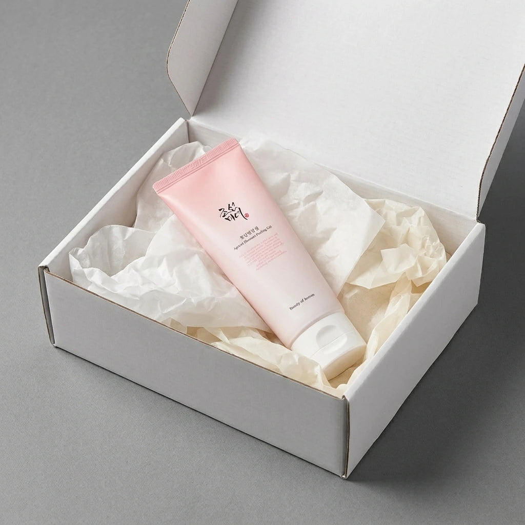 Angle : Vue oblique dynamique à mi-hauteur.  Scène : Le tube de l'image est présenté à l'intérieur d'un coffret de livraison premium e-commerce en carton blanc mat ouvert. Le produit est niché au milieu d'une superposition esthétique de papiers de soie froissés de deux nuances : blanc laiteux et crème.  Fond & Lumière : Surface de studio mate et contemporaine grise. Éclairage uniforme et très lumineux de studio, mettant en valeur l'aspect cadeau exclusif et personnalisé du produit. (gemini-3-pro-image-previ