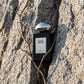 Concept de shooting : Traiter le packaging noir et argenté comme un élément d'architecture incrusté dans la nature.  Le Prompt à copier :  Une photographie de produit e-commerce originale. La boîte texturée noire fermée du parfum "BLACK EMPIRE" de Gris Montaigne Paris, arborant son logo argenté, est insérée verticalement dans la fissure naturelle d'une falaise de granit gris clair et brut. Une vigne sauvage sans feuilles s'enroule subtilement autour du packaging. Le contraste est fort entre la pierre claire