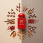 Concept de shooting : Une vue de dessus structurée mariant le packaging aux éléments de sa pyramide olfactive.  Le Prompt à copier :  Une vue de dessus (flat-lay) géométrique et artistique pour catalogue de luxe. La boîte rouge fermée de "ROUGE ABSOLU" est positionnée au centre d'une surface mate bicolore. Tout autour du packaging, les ingrédients bruts du parfum sont disposés avec une précision millimétrée : des boutons de rose séchés, des éclats de bois précieux, des baies roses et des larmes d'ambre. Écl