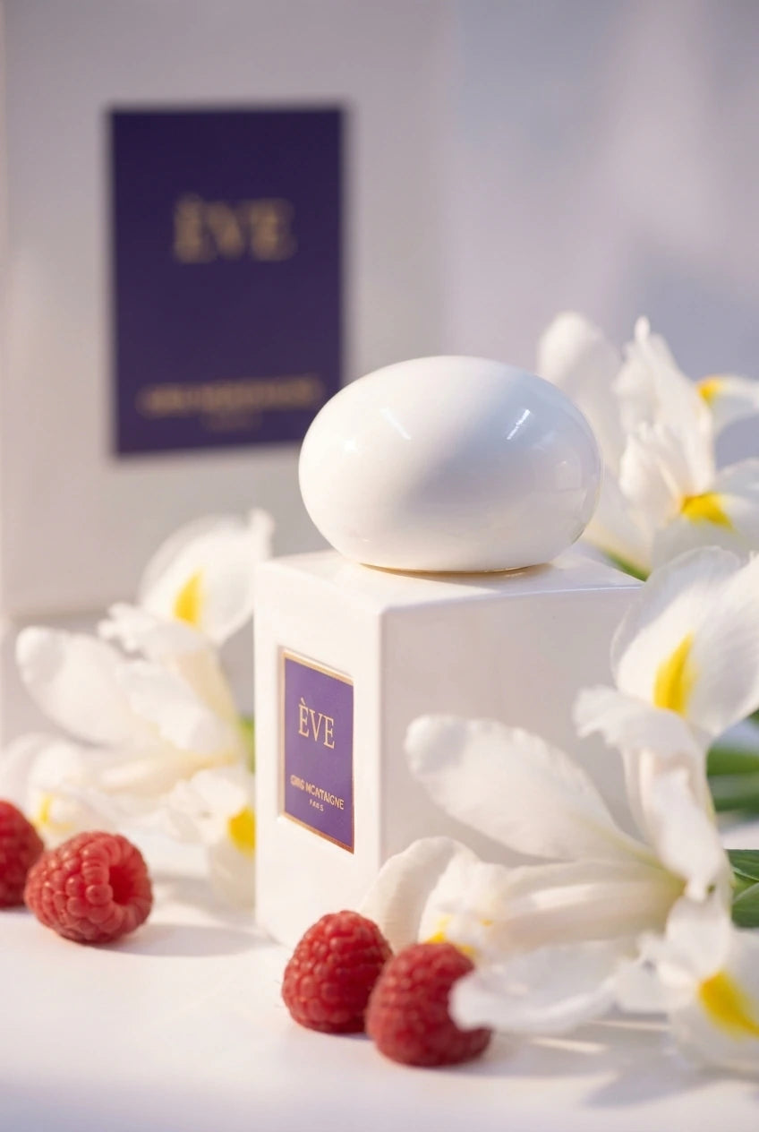Un plan serré de profil du flacon blanc épuré de image_3.png. Le capuchon sphérique blanc est le point central de la netteté. Il est entouré de véritables fleurs d'iris blancs et de quelques baies de framboise. La lumière est diffuse et douce, presque éthérée. La plaque violette est visible en arrière-plan flou (bokeh). Style : Photographie de beauté conceptuelle. (gemini-3-pro-image-preview)