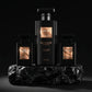 Un plan moyen net et frontal focalisé sur le grand flacon de gel douche et les deux bouteilles de parfum de image_221fc1.jpg, isolés de leur boîte arrière. Les produits sont alignés sur un bloc de quartz noir brut. Un spot directionnel précis frappe directement les étiquettes or rose métallisées de image_221fc1.jpg, révélant leur éclat subtil et haut de gamme au milieu de l'opacité noire. Style : Photographie cosmétique de haute précision. (gemini-3-pro-image-preview)