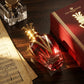 Un plan large oblique montrant le coffret et le flacon de image_ee1e0.jpg disposés sur un bureau en bois d'ébène verni. À côté d'eux, une partition de musique ancienne aux pages jaunies et un encrier en cristal sont visibles. Un pinceau de lumière rasante traverse horizontalement la scène, illuminant le jus rouge translucide du flacon et faisant vibrer les lettrages dorés de image_2ee1e0.jpg. Style : Campagne narrative cinématographique. (gemini-3-pro-image-preview)