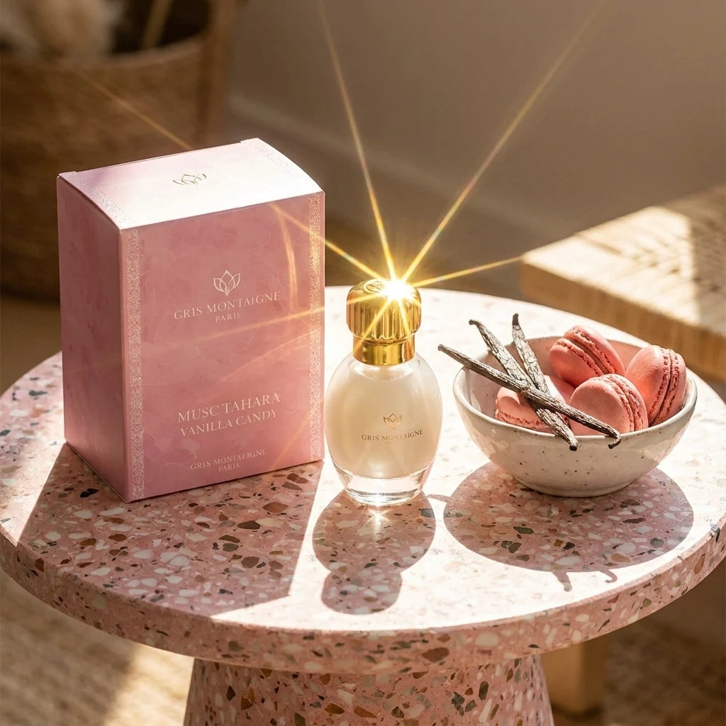 Un plan large oblique du coffret et du flacon de image_2fcb00.jpg disposés sur une table d'appoint moderne en terrazzo rose et blanc. À côté des produits, une petite coupelle artisanale en porcelaine contient des éclats de gousse de vanille et des macarons roses. Un rayon de soleil réaliste traverse la composition, créant un éclat brillant intense sur le capuchon doré de image_2fcb00.jpg. Style : Campagne publicitaire lifestyle et gourmande. (gemini-3-pro-image-preview)