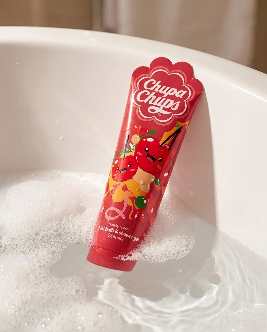 A slight high-angle commercial photograph of a 236ml bottle of "Chupa Chups Cheeky Cherry 2-in-1 shower gel" floating gently in a white porcelain bathtub. The tub is filled with clear water and soft, rich white soap bubbles clustered around the bottle. Calm water ripples. Warm, luxurious bathroom ambient lighting, professional studio setup, sharp details on the product, real life photography, no illustration --ar 4:5 (gemini-3-pro-image-preview)