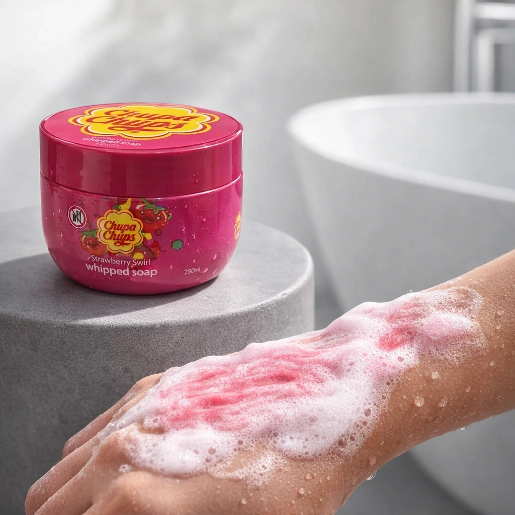 Side profile product photography. A 250ml Chupa Chups Whipped Soap jar is placed on a modern concrete stool next to a freestanding bathtub. In the foreground, a close-up of a person's forearm showing the product in use, lathered into a rich, velvety pink and white soap foam with real water droplets on the skin. Authentic, clean, commercial skincare ad, daylight, high-speed photography capturing water texture. --ar 4:3 --style raw (gpt-image-1.5)