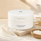 Creative e-commerce shot of the Beauty of Joseon Radiance Cleansing Balm jar inspired by image_464cc4.jpg. The white jar rests elegantly on a flat, cream-colored stone platform, surrounded by a smooth, glossy swirl of a melting white sorbet-textured balm and a small wooden bowl filled with white rice grains. The background is a soft, blurry warm ivory and light beige gradient under gentle morning sunlight. Radiance-boosting, clean, and organic luxury skincare concept. Aspect ratio 1:1, size 1200x1200px. (gp