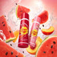 A dramatic low-angle shot looking up at the 'Chupa Chups - Watermelon Mix & Peach Pulp - Lip Balm' sphere floating in mid-air. The product appears heroic and monumental against a dynamic, animated background of swirling fresh watermelon slices, black seeds, and juicy peach halves splashing in crystal clear water. The lighting is bright and vibrant, making the balm packaging glisten. The style is a mix of commercial product photography and high-end 3D motion graphics. Intense colors, fresh vibe, hyper-detail